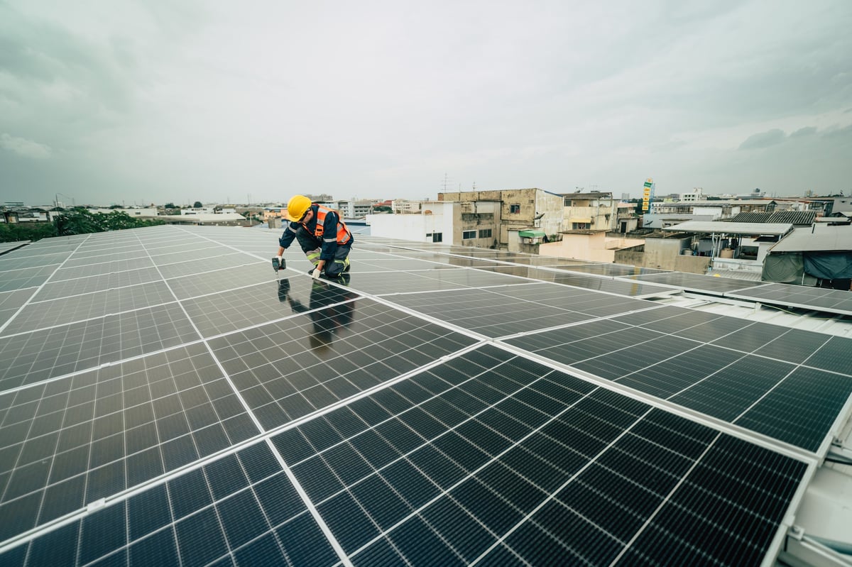 A technician carefully installs solar panels on a rooftop, surrounded by a bustling urban landscape