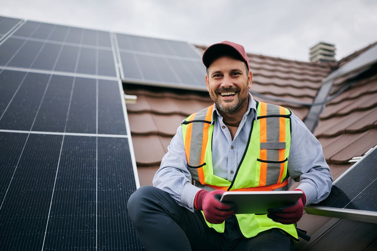 Happy worker using digital tablet during solar panels maintenance and looking at camera