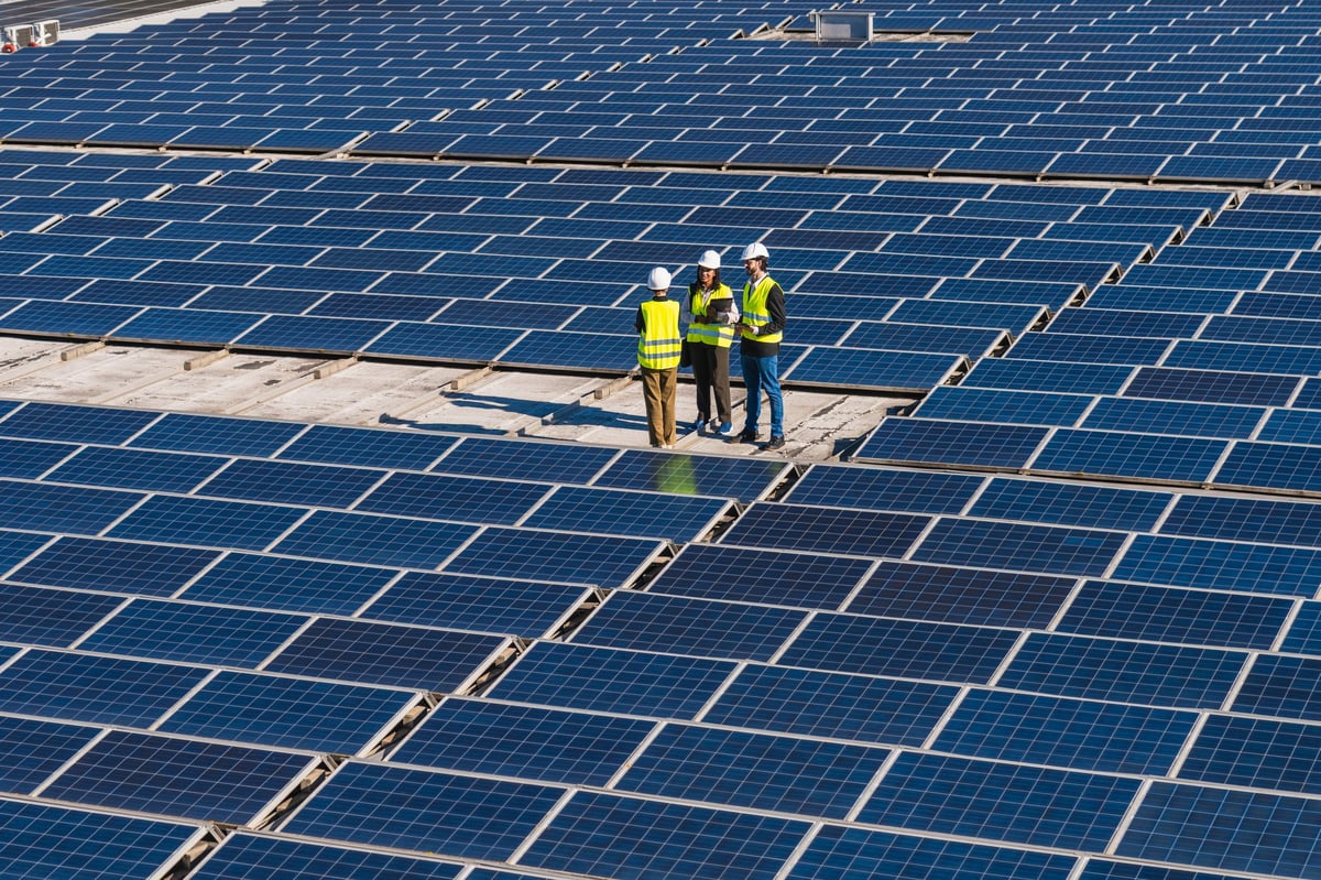 Engineers in hardhats and vests inspecting a vast rooftop solar panel array, discussing renewable energy and sustainable power